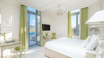 A bedroom with a large bed, a desk, a chair, a TV, and a balcony with curtains.