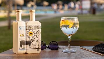 Two bottles of Black Pig Gin and a glass of cocktail on a wooden table with a blurred outdoor background.