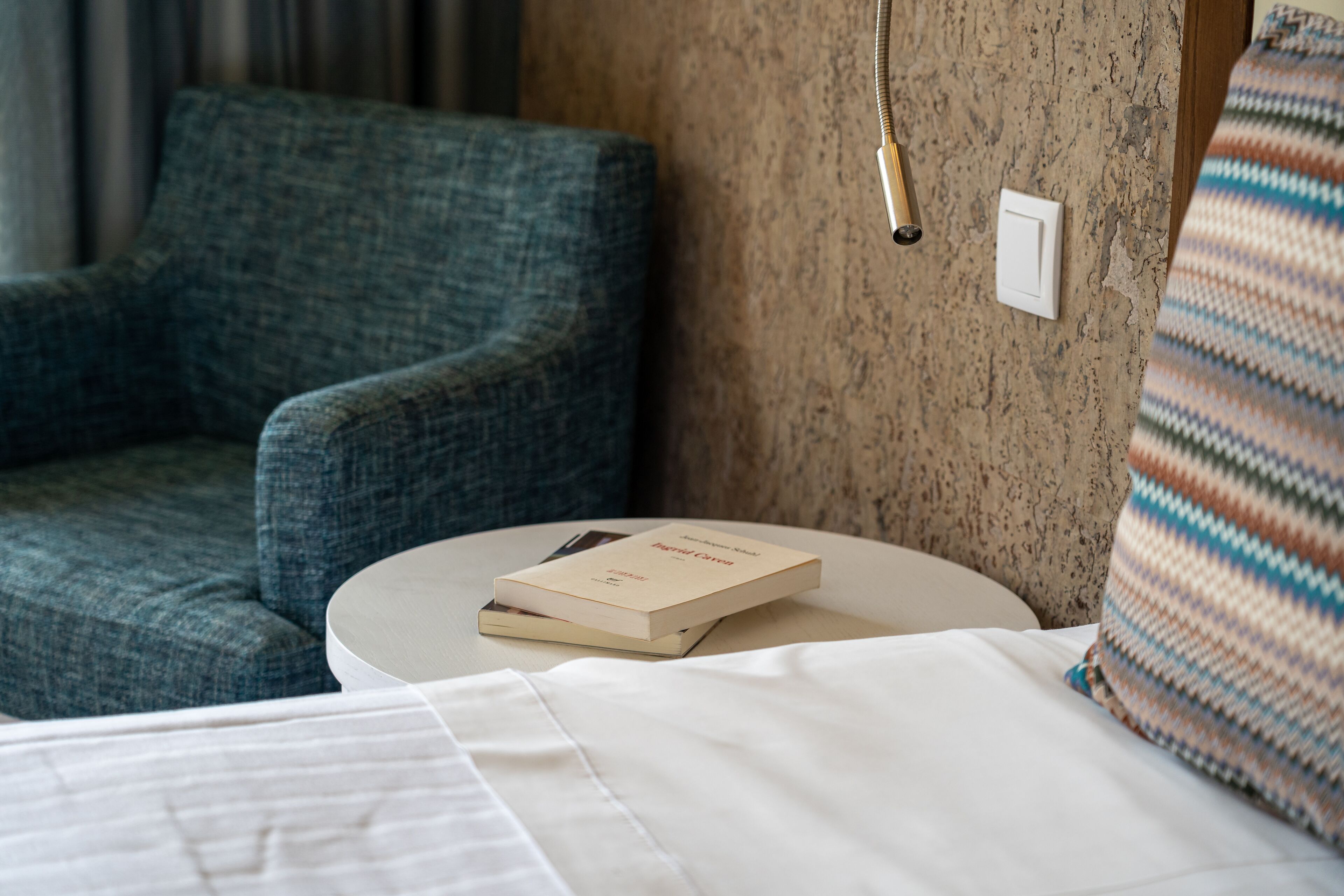 Una camera d'hotel con un letto, un tavolino rotondo, un libro, una sedia e una presa di corrente.