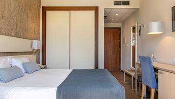A hotel room with a bed, bedside table, lamp, and a desk with a chair.