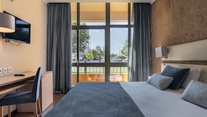 Quarto de hotel com cama, escrivaninha, cadeira, televisão e vista para o exterior.