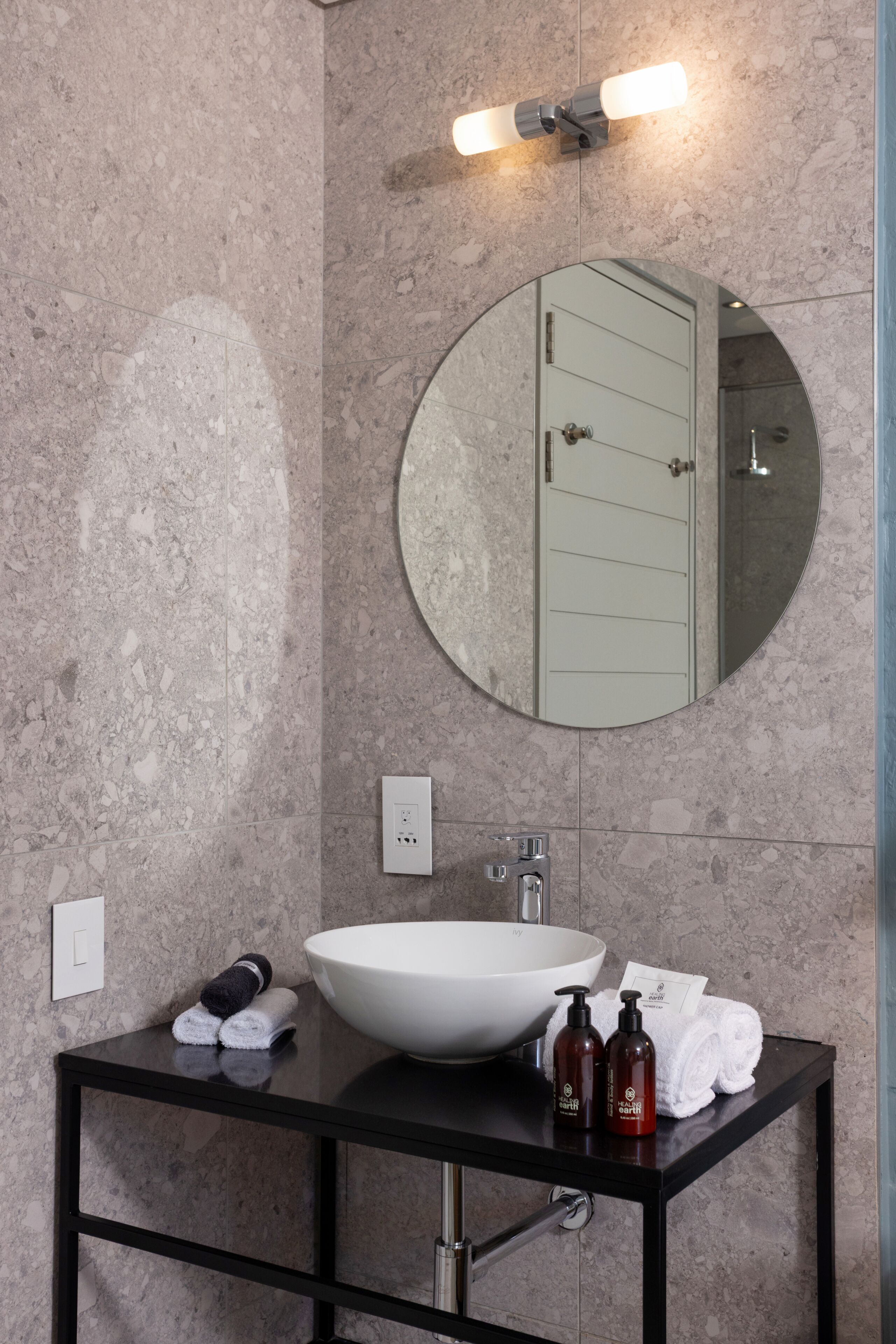 A bathroom with a round mirror, a white sink, a black vanity, and a towel rack.