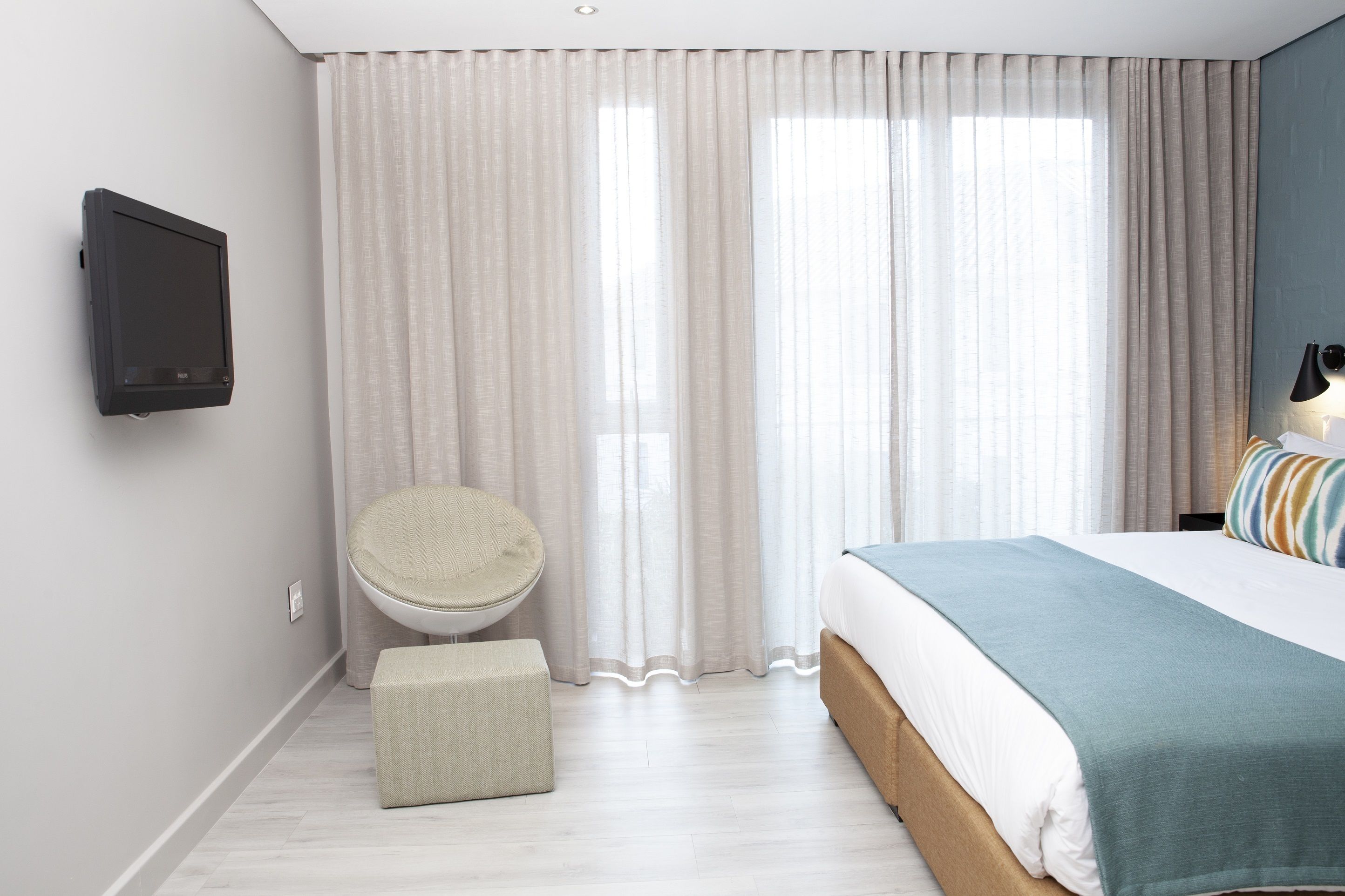 A modern bedroom with a bed, a round chair, a small ottoman, and a TV mounted on the wall.