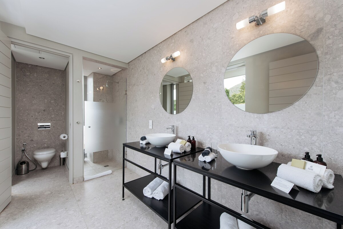 A modern bathroom with a large black vanity, two round mirrors, a white sink, and a toilet.