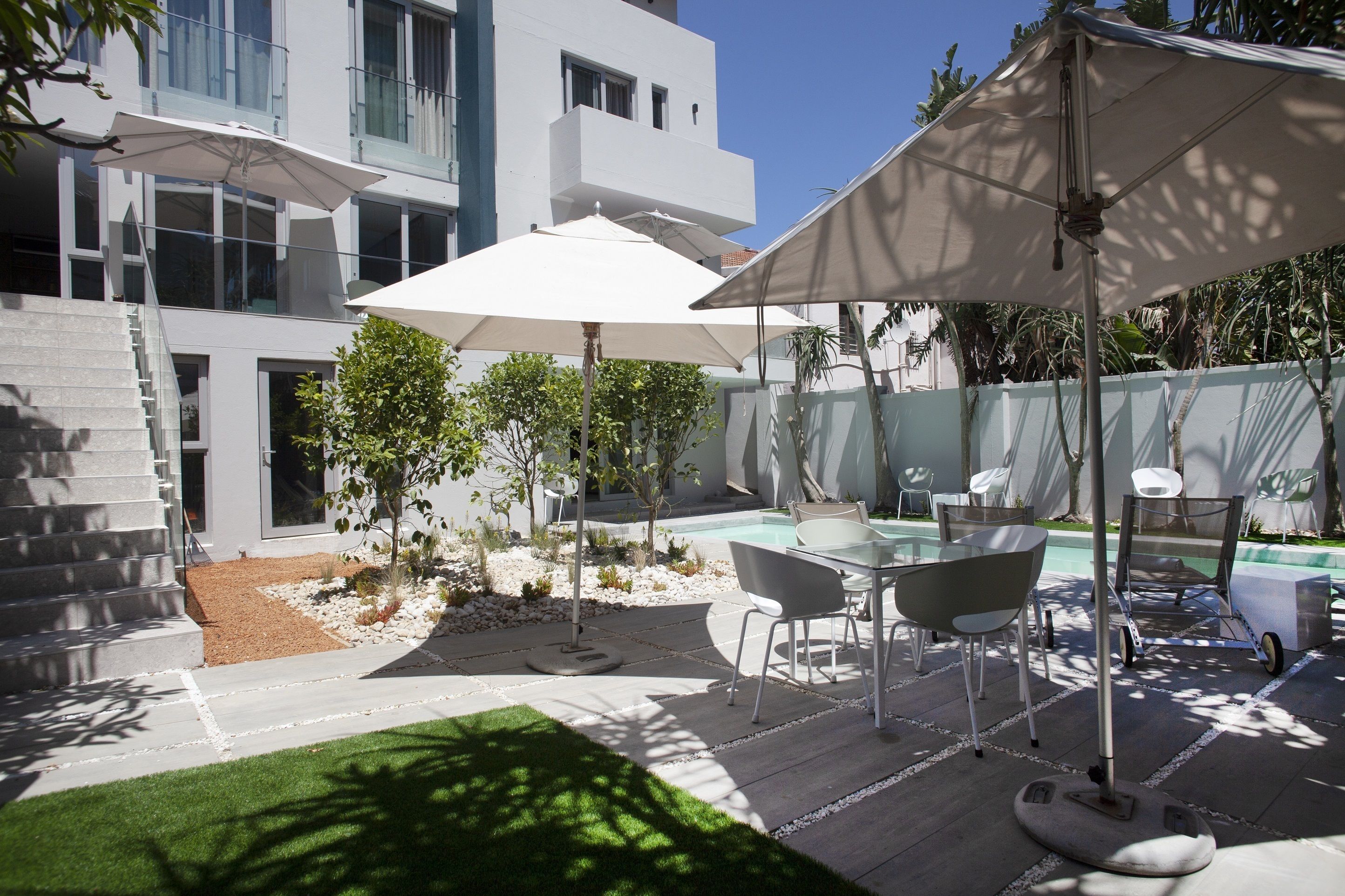 A modern outdoor patio with a pool, white umbrellas, and a dining area with chairs.