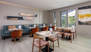 Un comedor moderno con un sofá azul, sillas naranjas y mesas dispuestas para el servicio.