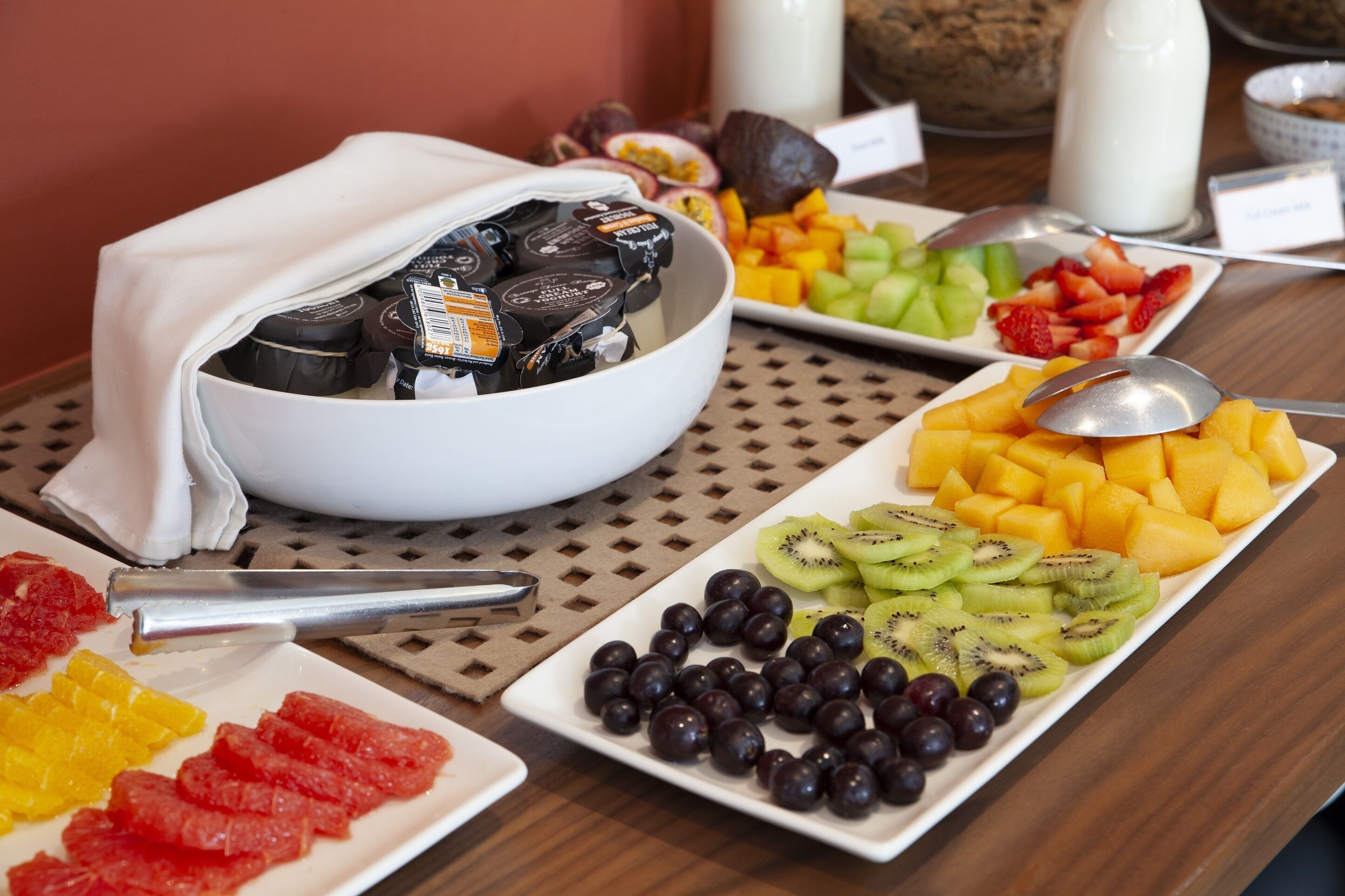 A breakfast buffet with various fruits, yogurt, and a bowl of chocolate spreads.