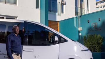 Uma carrinha branca estacionada em frente a um edifício moderno com uma parede de destaque azul-esverdeado e um letreiro que diz 'zest boutique hotel'.