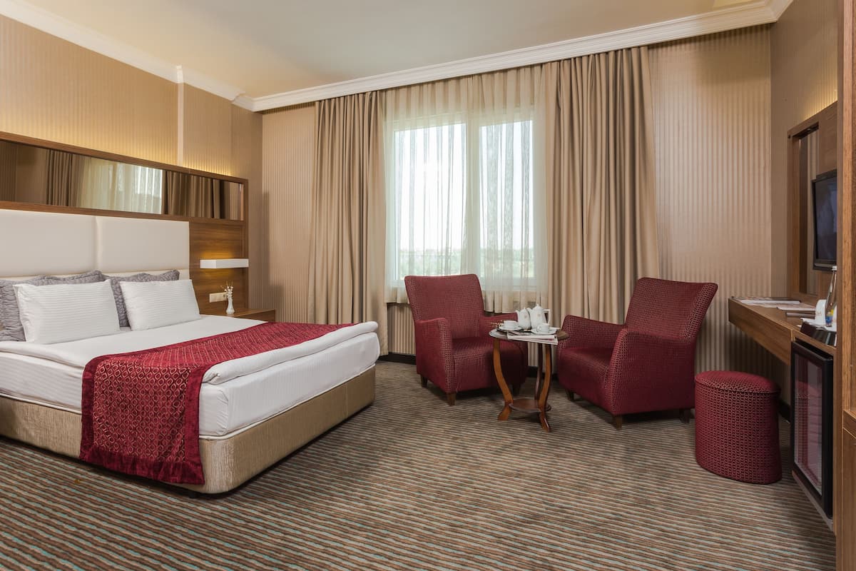 A hotel room with a large bed, two armchairs, a small table with a tea set, and a television.