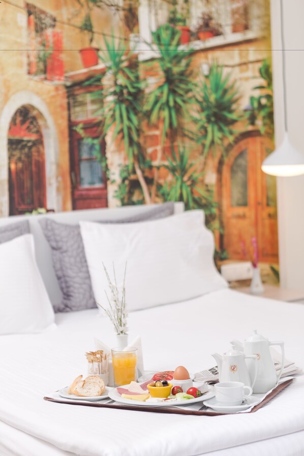 A neatly made breakfast tray on a bed with a mural of a building and plants in the background.