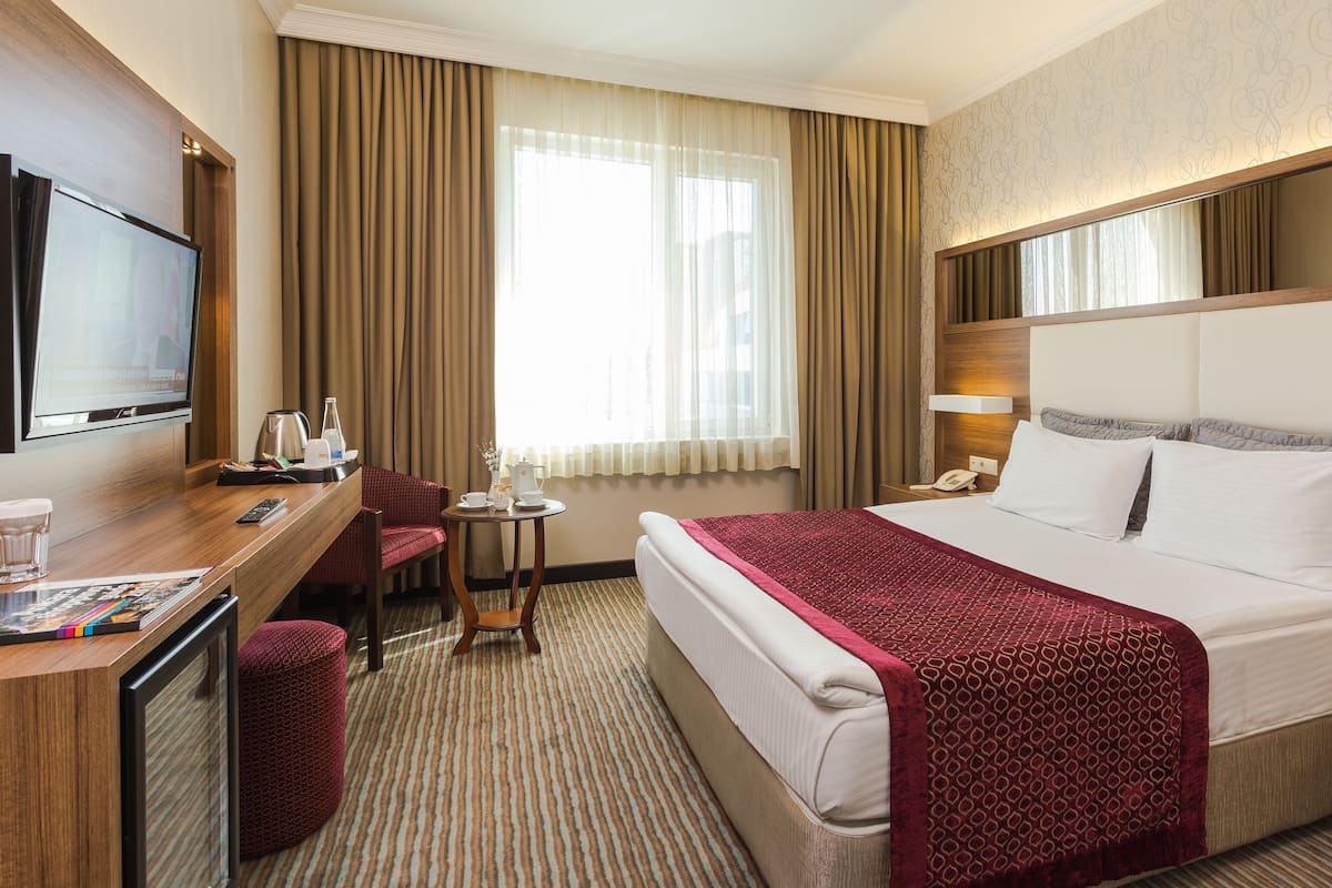 A hotel room with a bed, a desk, a TV, a chair, a small table, and a window with curtains.
