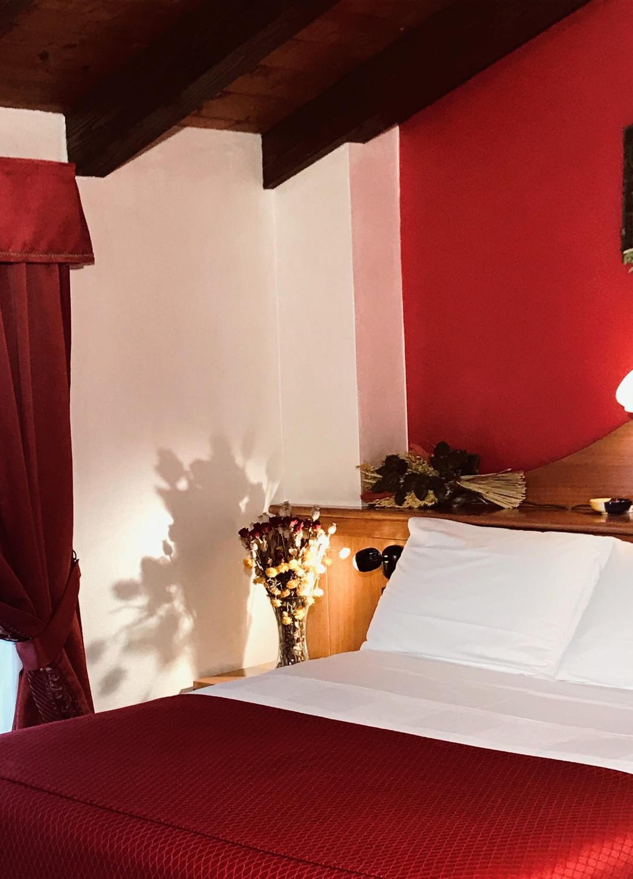 A bedroom with a bed, a wooden headboard, a nightstand with a vase of flowers, and a red curtain.