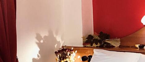 A bedroom with a bed, a wooden headboard, a nightstand with a vase of flowers, and a red curtain.