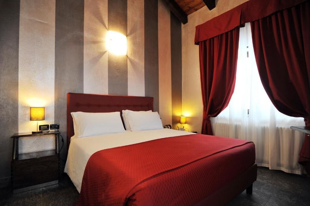 A hotel room with a large bed, striped walls, and red curtains.
