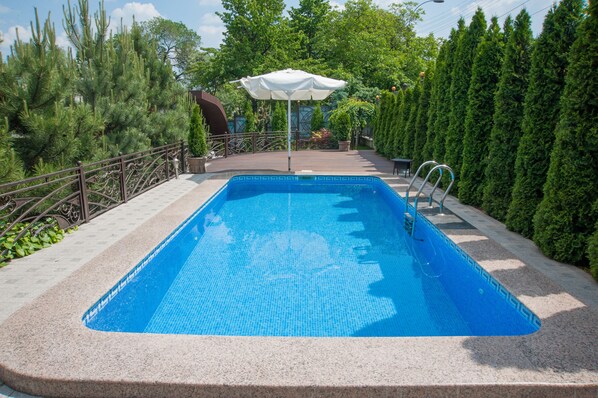 A rectangular swimming pool with a tiled edge, surrounded by a stone deck and metal railings.
