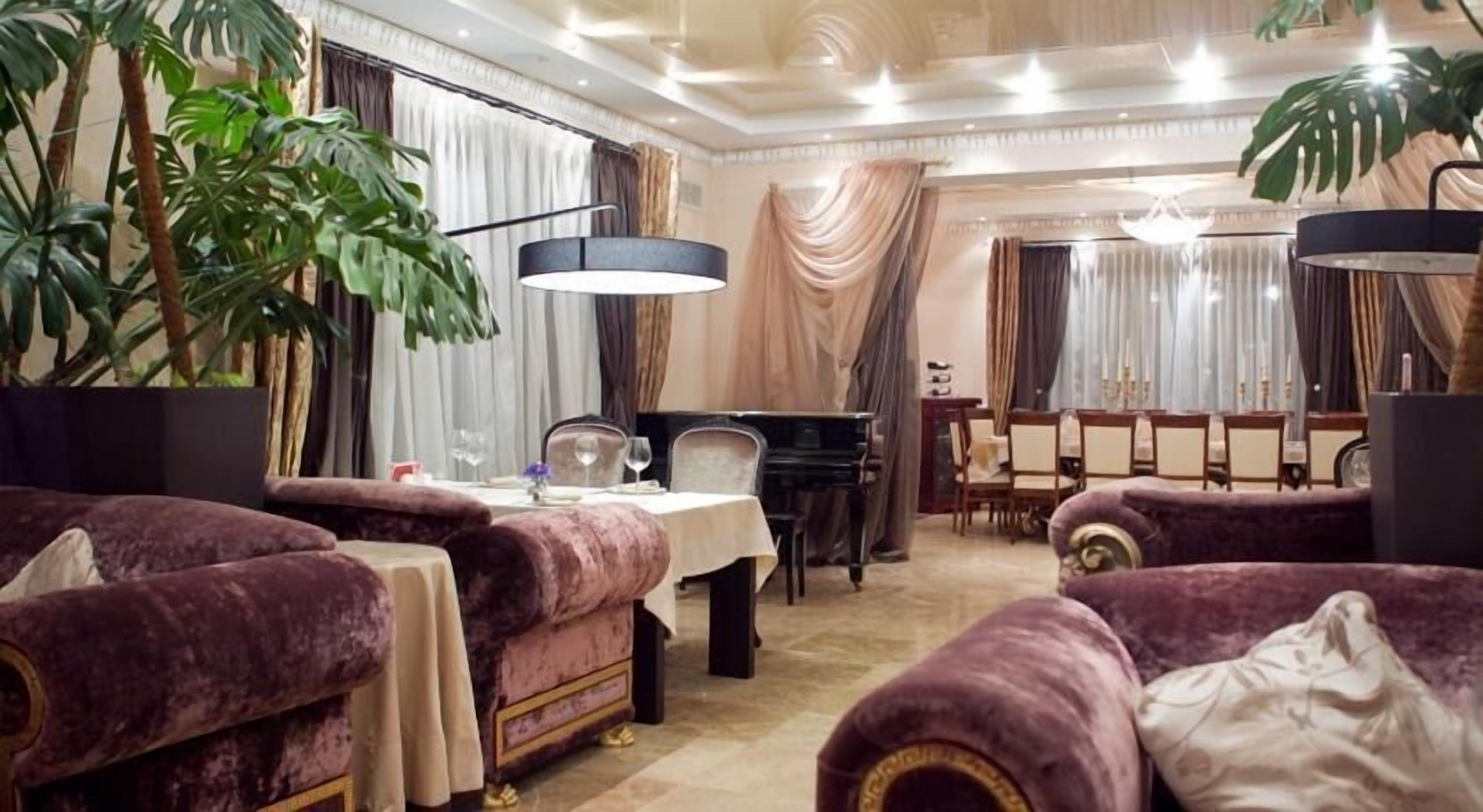 A luxurious room with plush purple sofas, a piano, and a dining area with a chandelier.