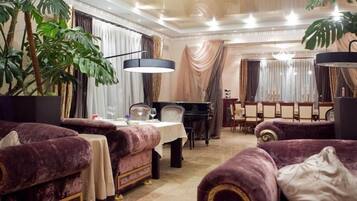 A luxurious room with plush purple sofas, a piano, and a dining area with a chandelier.