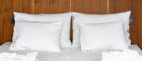 A neatly made bed with white linens and pillows, a wooden headboard, and a brown carpet.