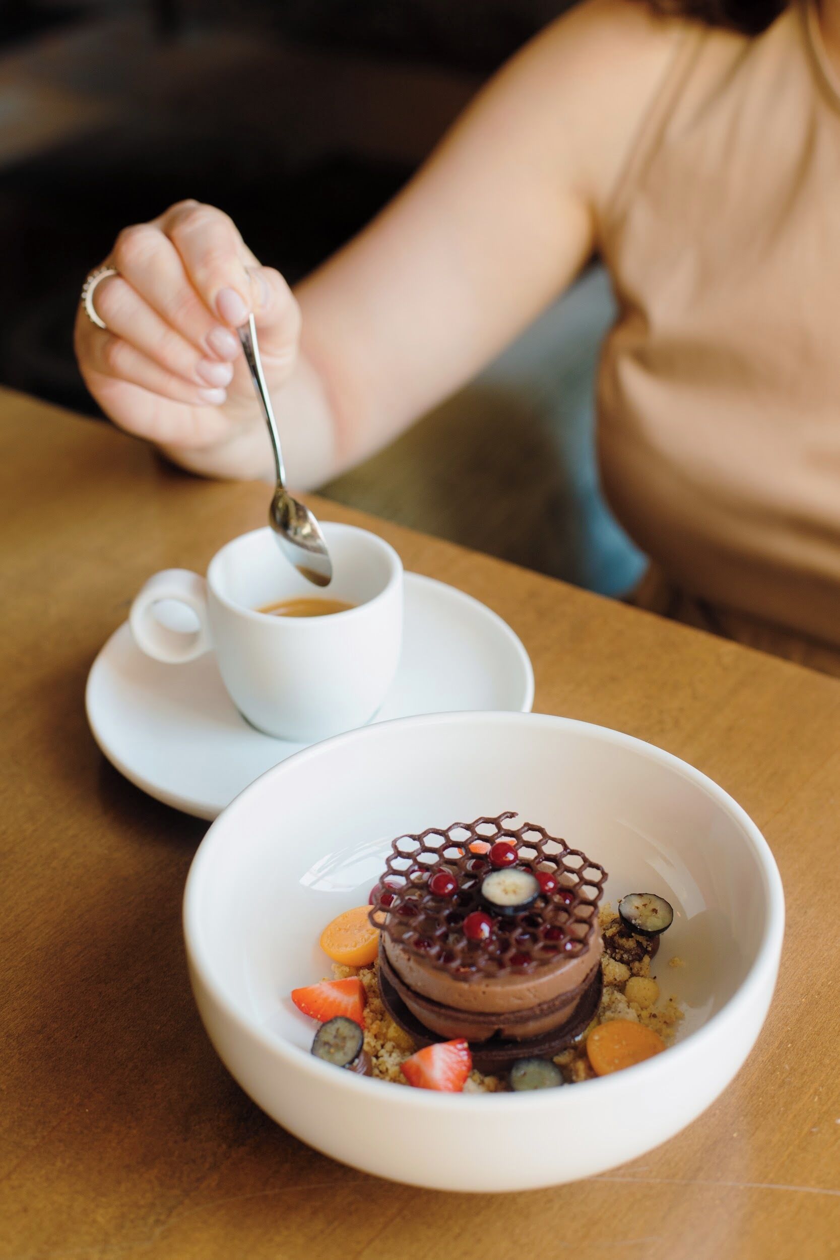 Un postre en un tazón con una cuchara, y una taza de café sobre un platito.