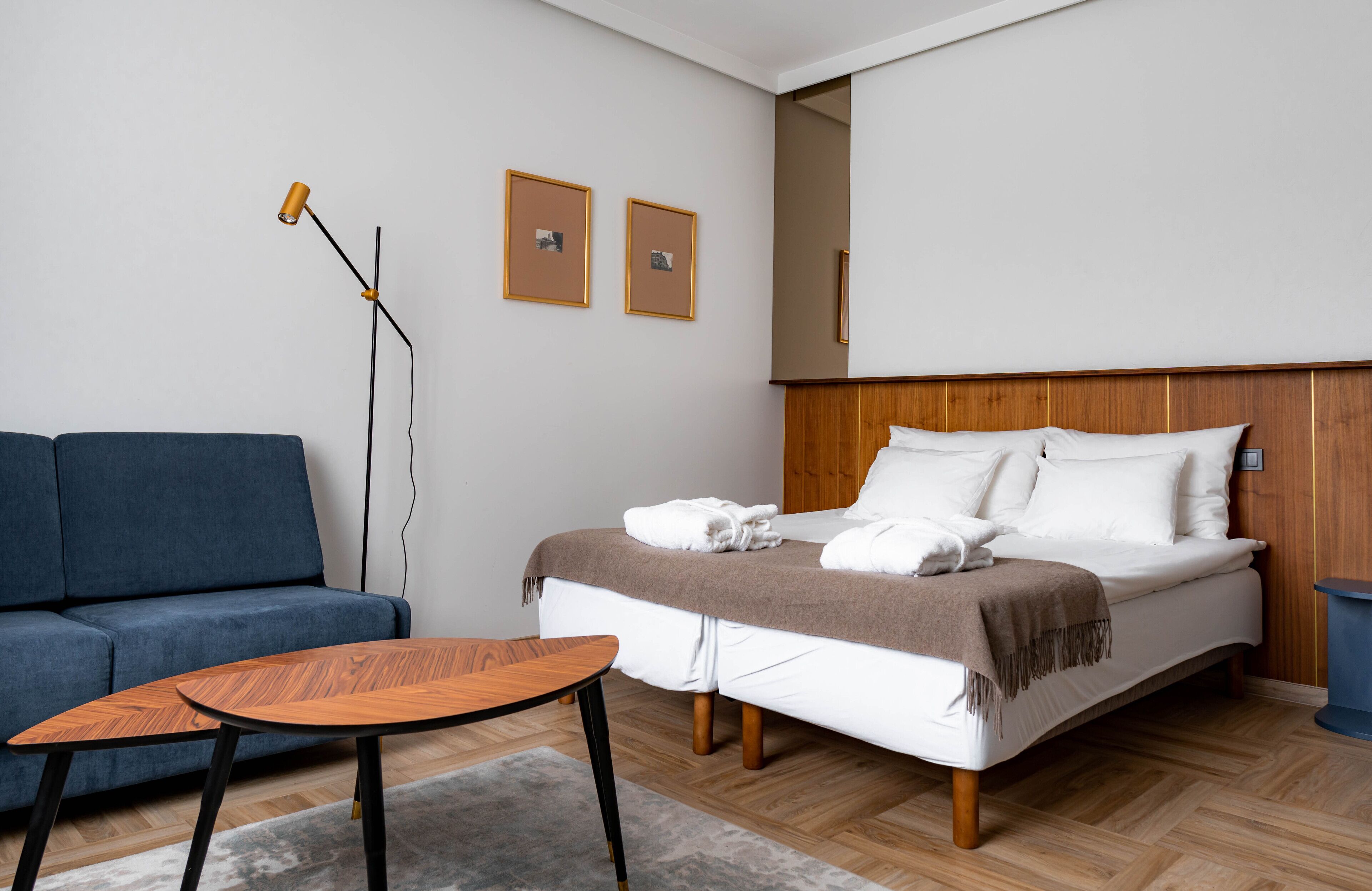 Ein modernes Hotelzimmer mit einem Bett, einem blauen Sofa, einem Holztisch und einer Stehlampe.
