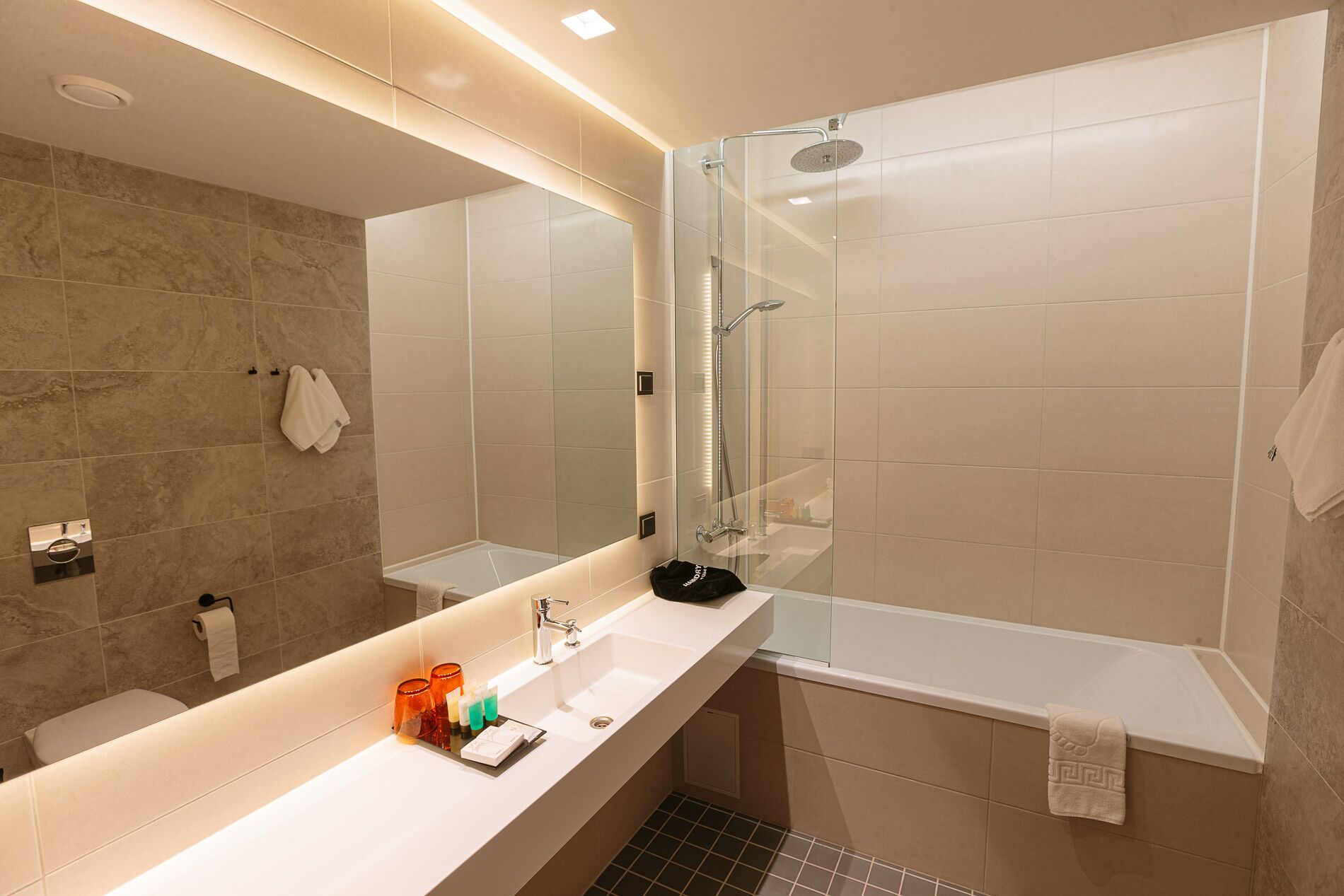 Un baño moderno con ducha envuelta en vidrio, un espejo grande y un tocador blanco con artículos de aseo.