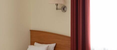 A hotel room with two beds, a wooden nightstand, a wall-mounted lamp, and a red curtain.