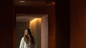 A person in a white robe standing in a hallway with wooden walls and a tiled floor. - Narva Hotell & Spa (Narva)