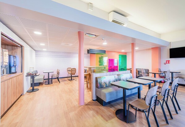 Un café moderno con suelo de madera, diversas opciones de asiento como mesas y sillas, y una decoración colorida.