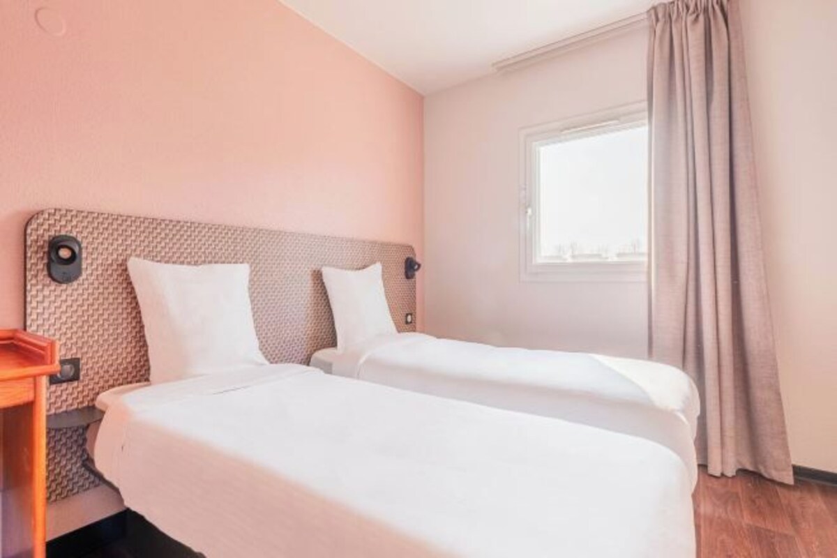 A hotel room with two beds, a window with curtains, and a wooden nightstand.