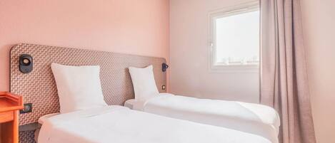 Une chambre d’hôtel avec deux lits simples, une table de chevet en bois, une fenêtre avec des rideaux et un mur orné d’un motif texturé.