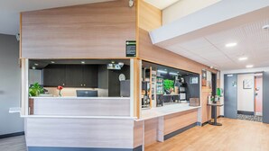 A reception desk with a wooden finish, a clock, and a plant. - B&B HOTEL Strasbourg Aéroport (Holtzheim)