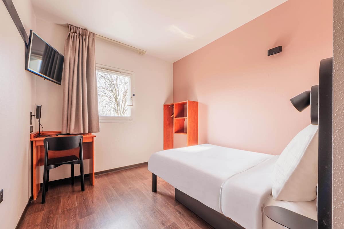 Una habitación con cama, escritorio, silla, televisor y ventana.
