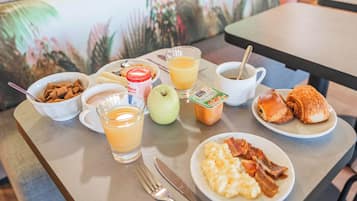 A breakfast table with cereal, juice, coffee, a croissant, an apple, and scrambled eggs.