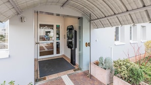 A modern building entrance with a glass door, a coffee machine, and a small garden area. - B&B HOTEL Strasbourg Aéroport (Holtzheim)