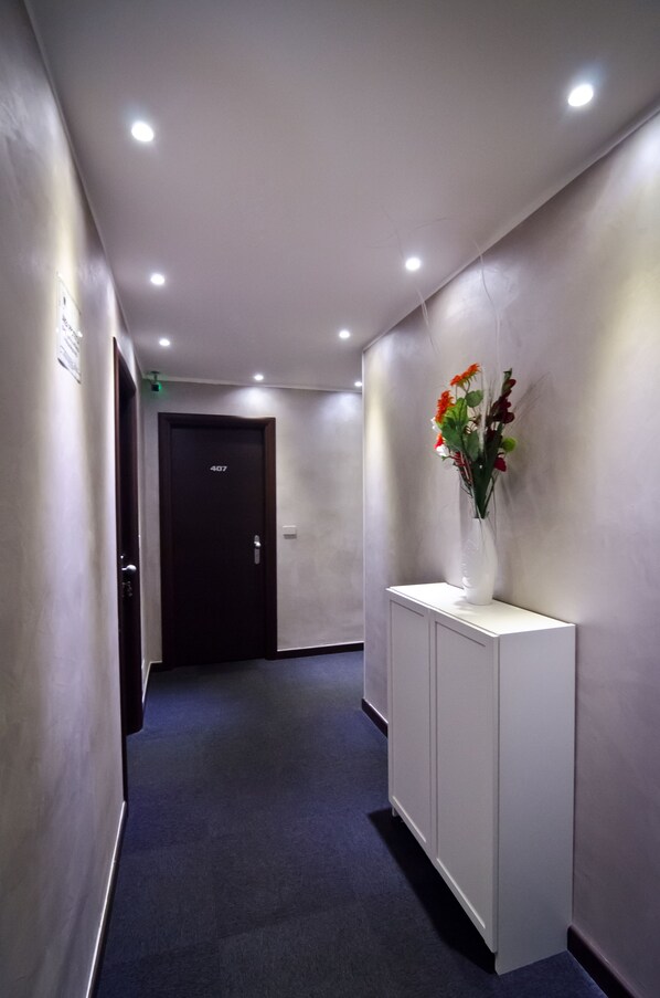Un pasillo con alfombra oscura, una consola blanca con un florero y una puerta con el número 407.