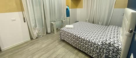 A bedroom with a bed, curtains, a TV, and a bedside table.