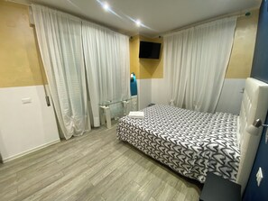 Un dormitorio con cama, cortinas, televisor y mesita de noche.