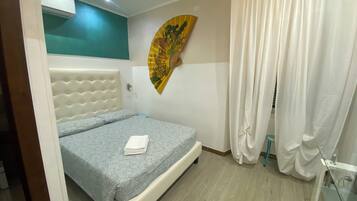 Un dormitorio con una cama, aire acondicionado instalado en la pared, un ventilador decorativo y una cortina.