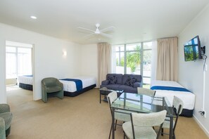 A hotel room with a glass table, two beds, a sofa, a chair, and a ceiling fan. - Alfresco Motor Lodge (Gisborne)