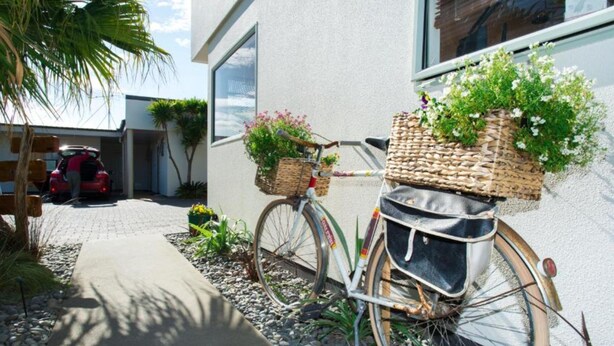 A bicycle with baskets, parked on a gravel path next to a building. - Alfresco Motor Lodge (Gisborne)