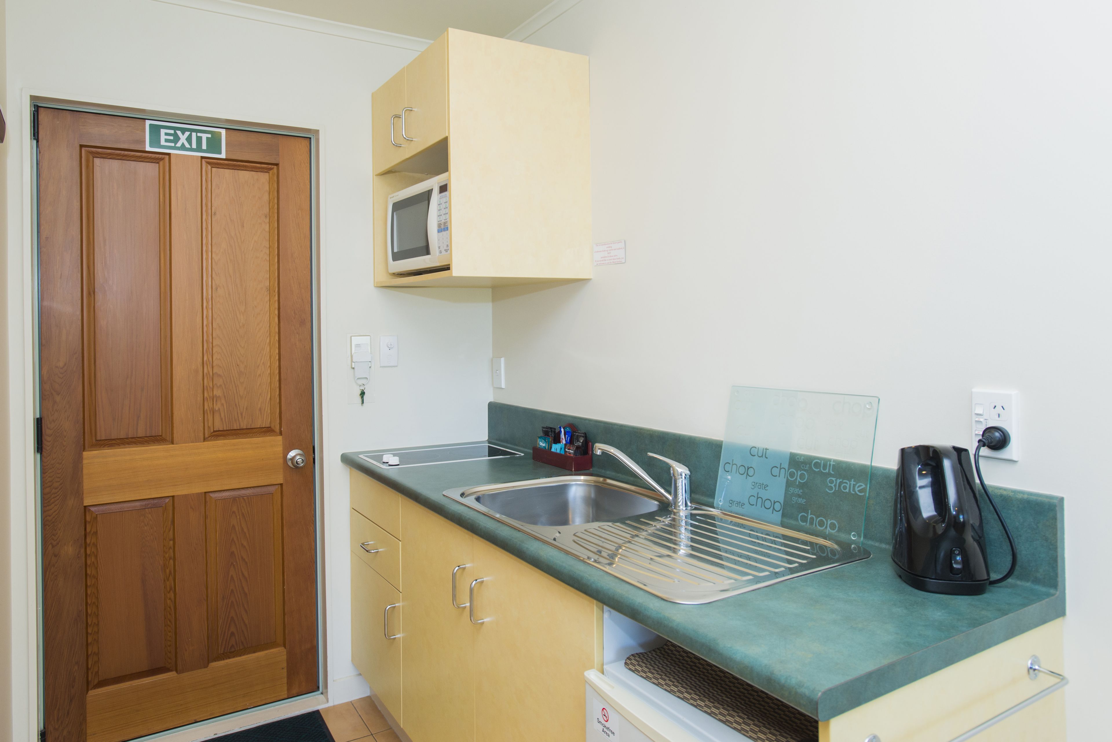 Una cocina con una puerta de madera marcada con la palabra 'EXIT', un microondas, una cafetera y una pizarra con escritura.