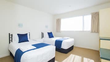 A hotel room with two beds, a large window with curtains, a carpeted floor, and a wardrobe.
