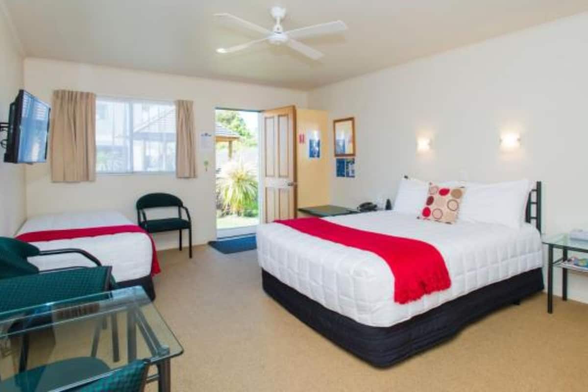 A hotel room with two single beds, a desk, a chair, a TV, and a ceiling fan.