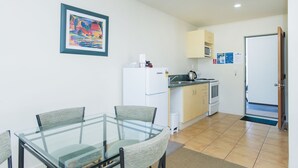 A compact kitchen with a refrigerator, microwave, and stove. There is a dining table with chairs and a framed picture on the wall. - Alfresco Motor Lodge (Gisborne)