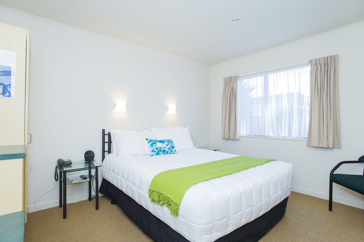 A hotel room with a bed, bedside table, lamp, and a window with curtains.