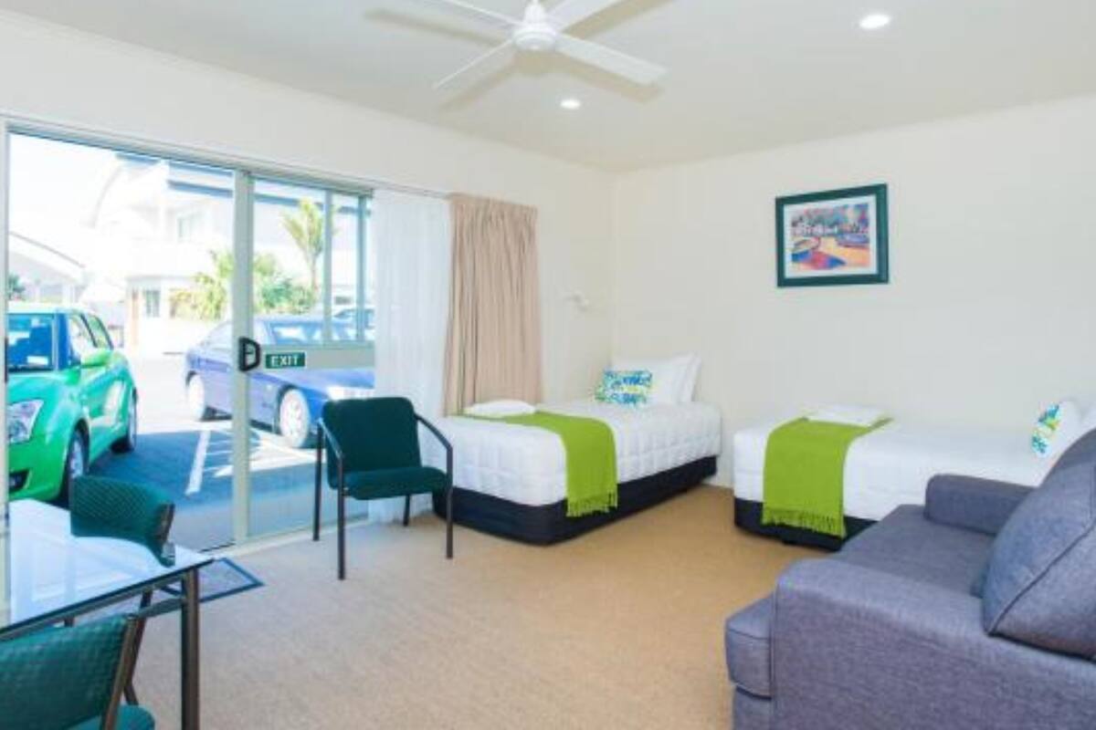 A hotel room with a bed, a sofa, a chair, a glass table, and a ceiling fan.