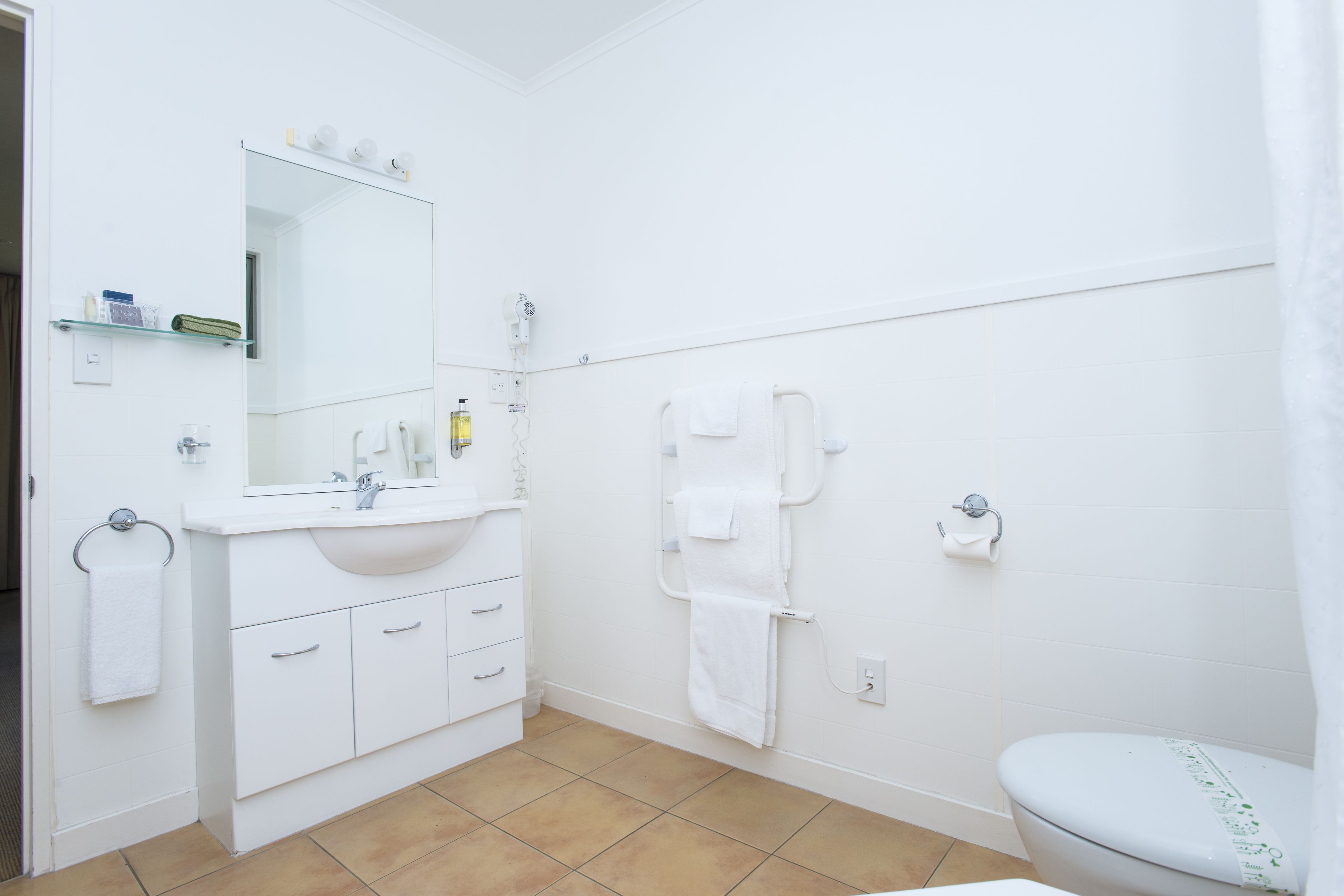 A bathroom with a white sink, mirror, and toilet. There are towels hanging on a rack and a shower curtain.