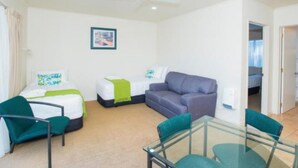 A modern hotel room with a bed, a sofa, a glass table, and a ceiling fan. - Alfresco Motor Lodge (Gisborne)