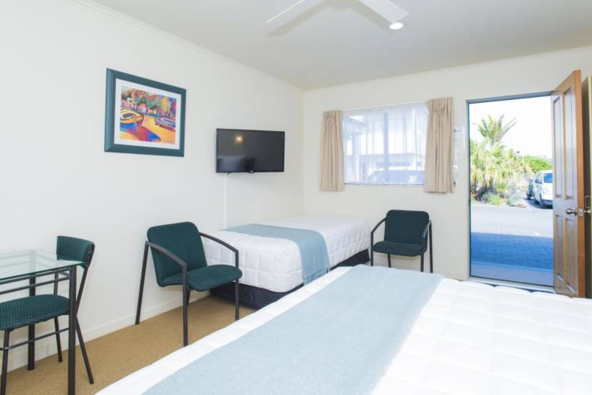 A hotel room with a bed, a desk, two chairs, a television, and a window with curtains.
