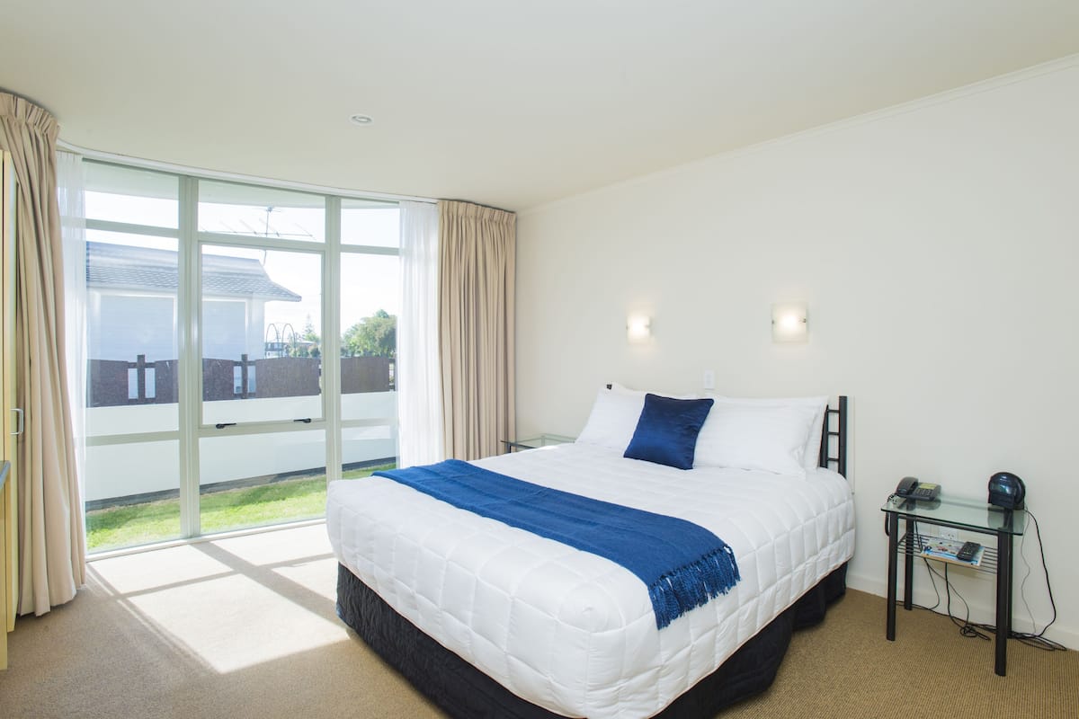 A bedroom with a large bed, a glass door leading to a balcony, and a small bedside table with a lamp.